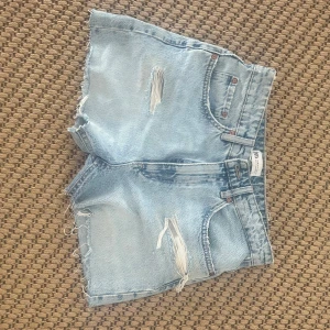 Zara  jeansshorts med slitningar - Säljer ett par ljusblå jeansshorts med råa kanter och slitna detaljer framtill. Klassisk femficksmodell med bälteshällor och hög midja. Oandvända 🩷💕