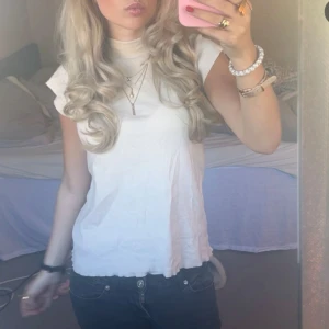 Vit ribbad polotopp - Säljer en vit ribbad polotopp med korta ärmar. Toppen har en tight passform och hög hals, perfekt att styla med smycken. Enkel och stilren design som passar till många outfits.