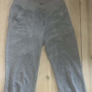 Grå mjukisbyxor från Juicy Couture - Säljer ett par grå mjukisbyxor från Juicy Couture med dragsko i midjan och stora fickor fram och bak. Byxorna har en klassisk, avslappnad passform och är perfekta för en chill stil.