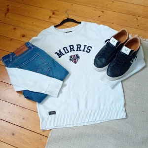 Vit stickad tröja från Morris - Vit stickad tröja från Morris Gents i storlek medium. Tröjan har rund halsringning, långa ärmar och broderad logotyp samt texten 'Morris' framtill. Ribbstickade muddar vid ärmslut och nederkant ger en klassisk look.