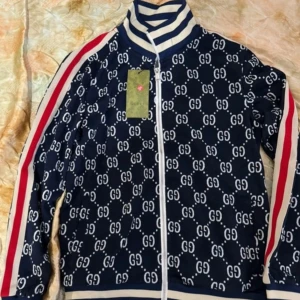 Mörkblå träningsbyxor med GG-mönster och rödvita revärer - Snygga mörkblå träningsbyxor med vitt GG-mönster över hela byxan och röda samt vita revärer längs sidorna. Byxorna har en sportig look och resår i midjan för skön passform.