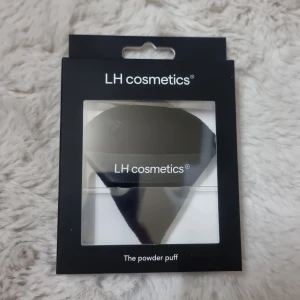 LH Cosmetics The Powder Puff - En svart, mjuk och trekantig powder puff från LH Cosmetics. Perfekt för att applicera puder jämnt i ansiktet och för touch-ups under dagen. Kommer i en stilren svart förpackning med transparent fönster. Vegansk och lätt att rengöra. Helt ny i förpackning.