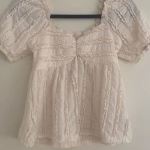 Beige volangblus med puffärm - Pris går att diskutera . Supersöt beige blus med puffiga korta ärmar och volangdetaljer över hela toppen. Den är aldrig använd . Den är stretchig och eftersom den ” svänger ut” på botten passar den Xs-S