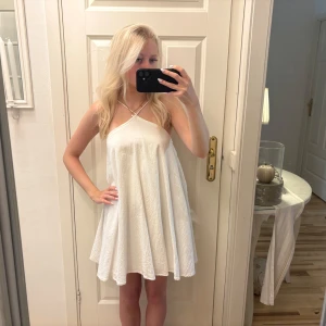 Vit kort sommarklänning med smala band - Superfin vit kort klänning med smala axelband som korsas framtill. Klänningen har en luftig och flowy passform, perfekt för varma dagar. Materialet är lätt och har en lite skrynklig struktur. Enkel och stilren design som känns fräsch och trendig.