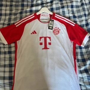 Bayern München Sané 10 Adidas matchtröja - FC Bayern München matchtröja från Adidas, storlek L. Vit med röda detaljer, kortärmad och slim fit. Sané 10-tryck på ryggen, klubbmärke och sponsorlogga framtill. Tillverkad i lätt och ventilerande funktionsmaterial, autentisk version säsong 23/24. Äkta köpt från Unisport. Priset är diskuterbart