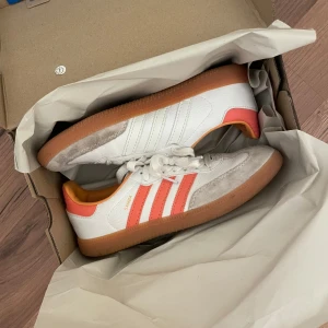 Adidas Samba vit/orange sneakers - Skitsnygga adidas samba i en cool orangeaktig färg. De är i övrigt väldigt väldigt bra skick, förutom ”fläckarna” på mockan som visas på bild, men dom är ingenting man egentligen tänker på. Storlek 39 och nypriset är 1300! Skickas i kartong☺️☺️