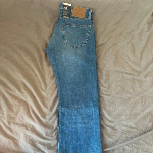Levi's 501 blå jeans straight fit - W32/L32 - Klassiska Levi's 501 jeans i blå denim med raka ben och femficksmodell. Jeansen har hög midja, knappgylf och den ikoniska läderpatchen bak. Perfekta för dig som gillar tidlös stil och vill ha ett par jeans som alltid funkar.