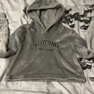 Grå fluffig hoodie från SHEIN - Supermjuk och fluffig grå hoodie från SHEIN med broderad text 'California West Coast' på bröstet. Tröjan har huva och lång ärm, perfekt för chill dagar. Oversized och cozy vibe, passar dig som gillar avslappnad stil.