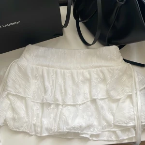 Vit volangkjol med broderi - Har inbyggda short inne!!! Free size, passar mig som är strl s. Aldrig använd , köpt utomlands. På båda sidor har drawstrings så man kan välja längd och knyta rosette. Superfin vit kortkjol med volanger och diskret broderat mönster. Kjolen har en luftig känsla och är perfekt för varma dagar. Söt och trendig modell som passar till många olika stilar.