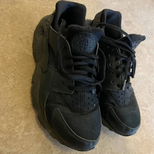 Svarta Nike Huarache sneakers - Säljer ett par helsvarta Nike Huarache sneakers med chunky sula och klassisk logga på plösen. Skorna har snörning och är tillverkade i en mix av skinn och syntetmaterial. Perfekta för dig som gillar en sportig och streetinspirerad look.