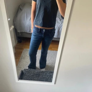 Blå bootcut jeans från Gina Tricot - Säljer ett par snygga blå jeans från Gina Tricot i storlek 158. Jeansen har bootcut-modell med lätt utsvängda ben och klassisk femficksdesign. Mörkblå tvätt och tillverkade i mjukt denimtyg med dragkedja och knapp framtill.