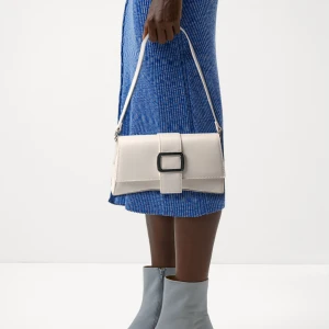 Vit axelväska från Even&Odd -  vit axelväska från Even&Odd. Väskan har en rektangulär form, justerbart axelband och en snygg detalj med silvrigt spänne framtill. Magnetlås och ett ljust innerfoder med ficka. 