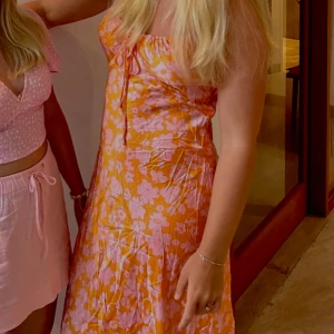 Blommig långklänning med snörning - Superfin långklänning i orange och rosa med blommigt mönster. Klänningen har smala axelband, söt snörning vid bysten som går att justera storlek. Klänningen köpte jag i Australien och är från märket Chanda. Materialet är i satin. Köptes för 700 kr säljer för 300💕💕