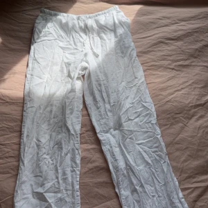 Vita linnebyxor med snörning - Luftiga vita linnebyxor med avslappnad passform och elastisk midja med snörning. Perfekta för varma dagar och chill vibes. Byxorna har raka ben och sidfickor för en enkel och clean look. 