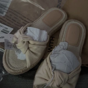 Beige sandaler med knut från H&M - Snygga beige sandaler från H&M i storlek 36. De har en platt sula, grov textil i bomull och en trendig knutdetalj framtill. Perfekta för varma dagar och ger en chill vibe till din outfit. Säljer då dem tyvär inte passar! De är slutsålda. 