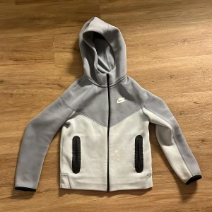 Nike blå hoodiejacka med dragkedja - Nike hoodiejacka i två nyanser av blå  med svart dragkedja och svarta detaljer vid fickorna. Jackan har huva, lång ärm och är tillverkad i mjukt material, perfekt för chill dagar eller träning. Klassisk Nike-logga på bröstet och sportig look.