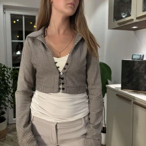Rutig croppad overshirt från Zara - Snygg tajt croppad overshirt från Zara i svartvitt rutigt mönster. Jackan har långa ärmar, klassisk krage och knäppning framtill med svarta knappar. Perfekt att styla med höga byxor för en trendig look. (Passar perfekt, orkade bara inte knäppa alla knappar).