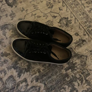 Lanvins  - Snygga svarta sneakers från Lanvin med coola lackade tår och klassisk vit sula. Skorna har snörning och en mix av mocka och glansigt material framtill. Perfekta för dig som vill ha en stilren men ändå unik look.
