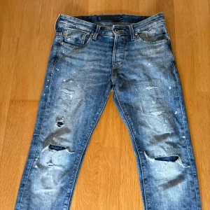 Jack and jones Glenn - Säljer ett par blå jeans från Jack & Jones modell slim glenn med coola slitningar, hål på benen och vita färgstänk. Liknande dsquared2 jeans storlek 29/30 Nypris 850kr
