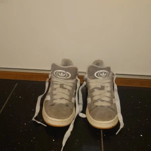 Gråa Adidas campus i mocka - Snygga gråa Adidas sneakers i mocka med högt skaft och klassisk vit Adidas-logga på plös och häl. Skorna har breda vita snören och vit sula med gummidetalj. Perfekta för dig som gillar streetstyle och vill ha en clean look. 450 kr eller bud.
