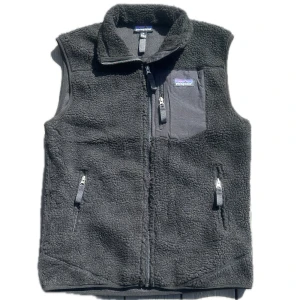 Svart fleeceväst från Patagonia - Mysig svart fleeceväst från Patagonia med hög krage, tre dragkedjeförsedda fickor och klassisk logga på bröstet. Västen har en enkel, stilren design och är perfekt att slänga på sig när det är kyligt ute.