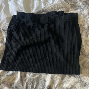 Svart ribbad kjol från ONLY - Svart ribbad kjol från ONLY i midilängd. Kjolen har en elastisk midja och är gjord i ett mjukt, stretchigt material som sitter snyggt på kroppen. Perfekt att styla med en oversized hoodie eller en tight topp. Kjolen slutar runt knäna 