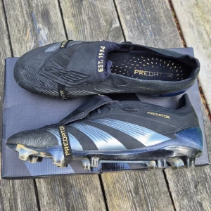 Adidas Predator fotbollsskor svart - Adidas Predator Foldover Tounge, hel svarta skor med FG dobbar. Skorna är i bra skick med minimala tecken på användning, med ingenting som kommer att påverka prestationen på planen. 