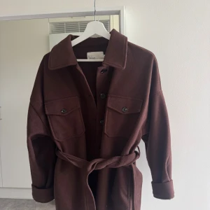 Brun jacka med knyte från  NLY Trend - Snygg brun jacka från NLY Trend med stora bröstfickor, knappar framtill och ett matchande bälte i midjan 🌸