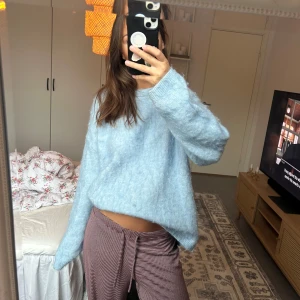 Ljusblå fluffig stickad tröja - Supermysig ljusblå stickad tröja med oversized passform och långa ärmar. Tröjan har en fluffig känsla och ribbade muddar vid ärmslut och halsringning. Perfekt för dig som gillar en chill och avslappnad stil.