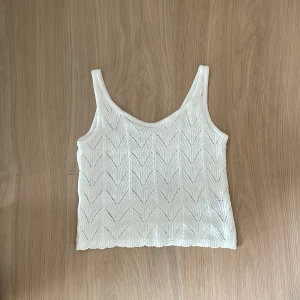 Vit stickad linnetopp med mönster - Supersöt vit stickad linnetopp från Cubus med snyggt hålmönster i sicksack. Toppen är ärmlös och har en croppad passform, perfekt för varma dagar. Mjuk och luftig, passar till jeans eller kjol för en chill look.🥰