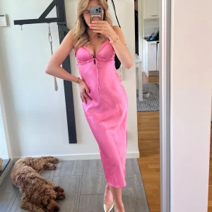 Rosa satinklänning med öppen rygg🩷 - Supersnygg rosa långklänning i satin med smala axelband, v-ringning och knyt framtill. Klänningen har en öppen rygg och en figurnära passform som ger en riktigt chic look. Perfekt för dig som vill sticka ut och känna dig extra glam. Använd 1 gång🩷