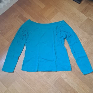 Turkos långärmad offshoulder-tröja  - Snygg turkos långärmad tröja från Åhlens med offshoulder-design. Tillverkad i mjuk bomull som känns skön mot huden. 🩷