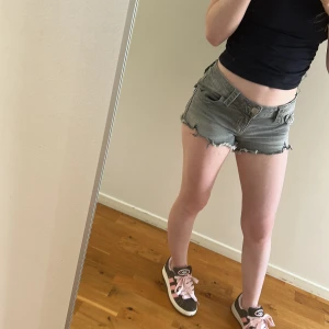 Grå jeansshorts med fransig kant - Snygga grå jeansshorts med låg midja och rå, fransig kant. Klassisk femficksmodell med coola bakfickor med knappdetalj.😍 supper snygga och ass sköna! Säljer på grund av att dem är för små för mig! Har vara användigt några få gånger!❤️