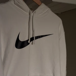 Nike tröja - Vit hoodie från Nike med stor svart Swoosh-logga på bröstet och coola neongula detaljer längs ärmarna. Klassisk känguruficka framtill, dragsko i huvan och mjukt material som känns skönt mot huden. 