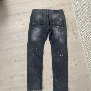 Svarta slitna jeans från jack & jones - Säljer ett par svarta jeans från Replay med coola slitningar och distressed detaljer framtill och baktill. Jeansen har rak passform och klassisk femficksdesign. Perfekta för dig som gillar en edgy streetstil.