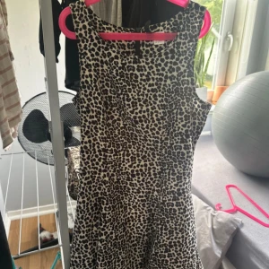 Svartvit leopardmönstrad klänning - Cool ärmlös kortklänning med svart leopardmönster på vit botten. Klänningen har rund halsringning och en lätt utställd passform som ger en snygg siluett. Perfekt för dig som vill sticka ut med ett djurmönster. Dragkedja i ryggen för enkel på- och avtagning.