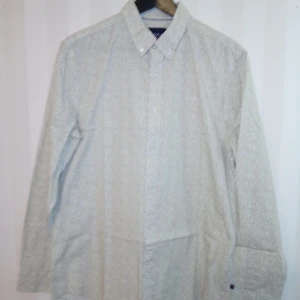 Vit blommig skjorta från Bondelid - Snygg vit skjorta från Bondelid med diskret blommigt mönster i ljusa färger. Klassisk krage, långärmad och tillverkad i mjuk bomull. Perfekt för dig som gillar stilrena men ändå unika detaljer. Knappar framtill och relaxed fit. Kan skickas med extra pris via post.