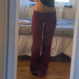 Vinröda vida byxor i mjukt tyg - Säljer ett par vinröda byxor med breda ben och låg midja. Byxorna har en loose fit och är gjorda i ett mjukt material som känns skönt mot huden. Perfekta för dig som gillar avslappnad stil och vill ha något som sticker ut lite extra.