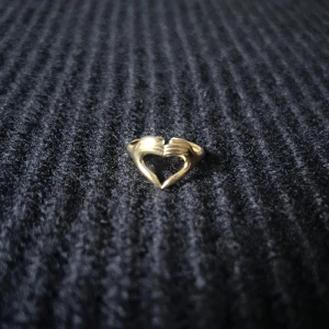 Mains d’Amour Doré – Golden Hands of Love Ring - Justerbar ring i rostfritt stål med guldplätering, rost- och nickelfri. Två händer förenas och omsluter fingret med en varm och symbolisk känsla av närhet