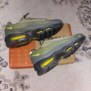 Nike corteiz Air Max 95 camo/olivgrön sneakers - Nike Air Max corteiz 95 sneakers i olivgrönt och grått med gula detaljer och camo-mönstrad plös. Skorna har synliga Air Max-bubblor, snörning och broderad gul logga på sidan. Ovandelen är i syntet och mesh för en sportig vibe. Perfekta för dig som gillar streetstyle.