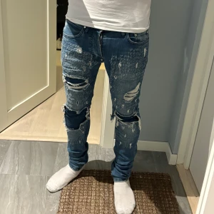 Blå slitna slim fit jeans Integral - Säljer ett par blå slim fit jeans från Integral med rejält slitna detaljer och stora hål på knäna. Jeansen har klassisk femficksdesign, dragkedjegylf och är tillverkade i stretchig bomull. Perfekta för dig som gillar en edgy streetstil.