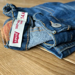 Levi's 502 blå jeans, regular tapered - Säljer ett par klassiska blå Levi's 502 jeans med regular tapered passform. Jeansen har fem fickor, snygga kontrastsömmar och knapp i metall framtill. Perfekta för dig som gillar en tidlös denimlook med lite smalare ben. OBS de är uppsydda innelängd 64 cm