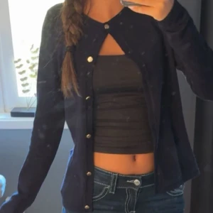 Mörkblå kofta med knappar - Snygg mörkblå kofta med guldiga knappar framtill. Koftan har lång ärm och en klassisk, enkel design som passar perfekt till jeans eller kjol. Materialet känns mjukt och lätt, vilket gör den skön att bära under både vår och höst.