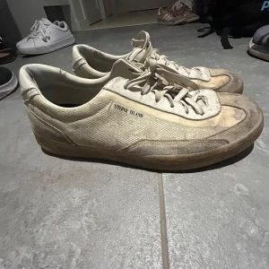 Vita sneakers från Stone Island -  vita sneakers från Stone Island med klassisk logga på hälen och sula. Skorna har snörning, ovandel i canvas och mockadetaljer samt gummisula. De går att tvätta bort smutsen på skorna. 