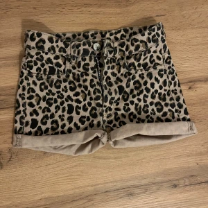 Leopardmönstrade shorts lågmidja - Snygga shorts med låg midja och med leopardmönster i beige och svarta toner. Modellen har klassisk femficksdesign, uppvikta benslut och dragkedja framtill. Perfekta för dig som vill sticka ut med en djärv stil i sommar.
