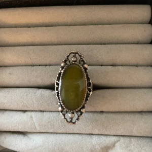 Vintage silverring med grön sten - Cool vintage ring i silverfärg med en stor oval grön sten i mitten. Ringen har detaljerad, nästan bohemisk ram runt stenen som ger en unik och retro vibe. Perfekt statement piece för dig som gillar att sticka ut.