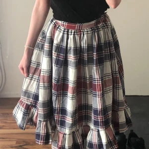 Rutig långkjol med volangkant✨ - Superfin långkjol med rutigt mönster i vinrött, blått och vitt. Kjolen knäppes med hyskor och hakar i midjan och en bred volang längst ner som ger en cool och avslappnad vibe. Perfekt för dig som gillar en lite bohemisk och chill stil.🌷(Midjemått ca 65cm)