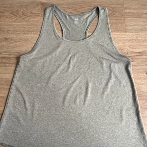 Grå linnetopp från H&M Sport - Säljer en grå linnetopp från H&M Sport i mjukt och stretchigt material. Modellen har brottarrygg och är perfekt för träning eller chill dagar. Enkel och stilren design som är lätt att matcha med andra plagg.