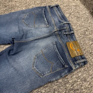 Jacob Cohën Jeans (Krobbes från GUTTASHOW) - Snygga blå jeans från Jacob Cohen med klassisk femficksdesign, bruna kontrastsömmar och läderpatch bak i midjan. Jeansen har raka ben och subtila slitningar framtill för en cool, avslappnad look. Tillverkade i mjukt denimtyg med knappgylf. Style 688! Just den byxa har Krobbe burit på Guttashow, ”10 Damer vs Krobbe” se för passform! Bra skick. 1045kr + frakt! Välmött, BB🍾