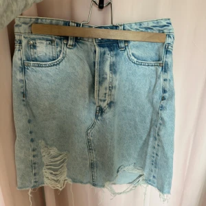 Ljusblå jeanskjol från &Denim - Ljusblå jeanskjol från &Denim i klassisk femficksmodell. Kjolen har slitna detaljer, rå kant nertill och knäppning med silverfärgade knappar framtill. Perfekt för dig som gillar en avslappnad och trendig stil.